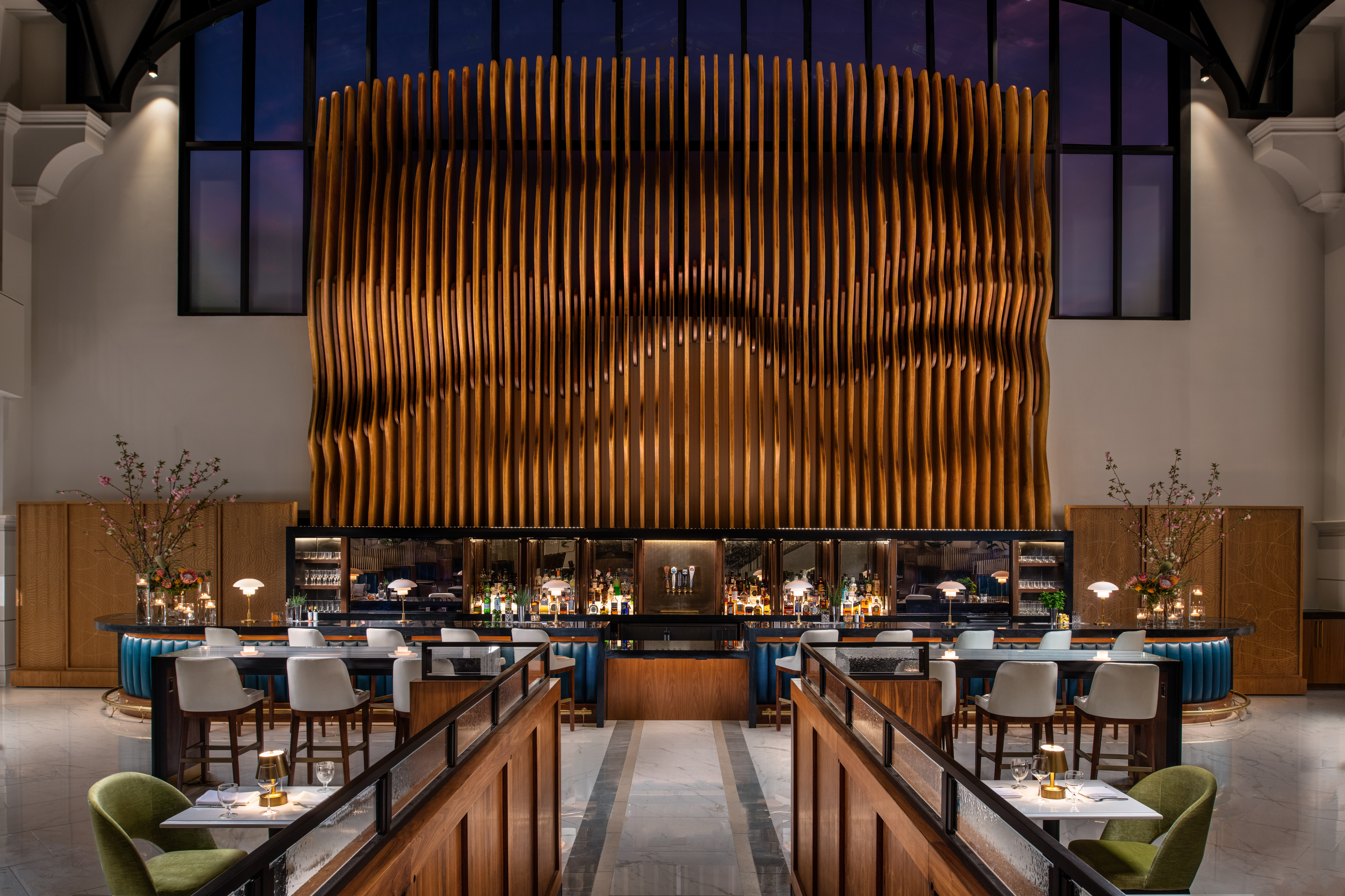 A long, modern dining hall with rows of tables and chairs facing a large, textured wooden wall.
