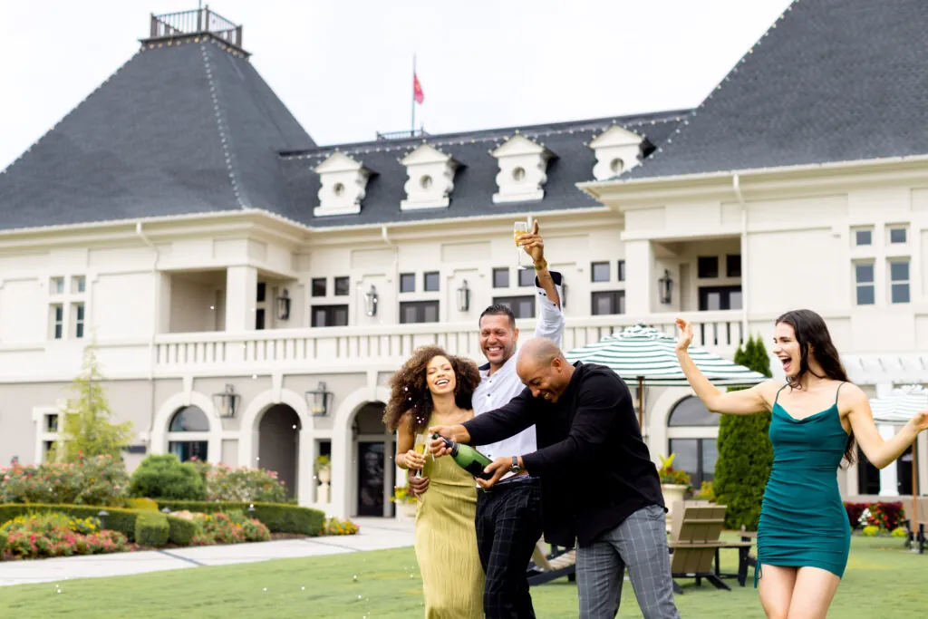 A group of people cheering with champagne bottles in front of a large white building.