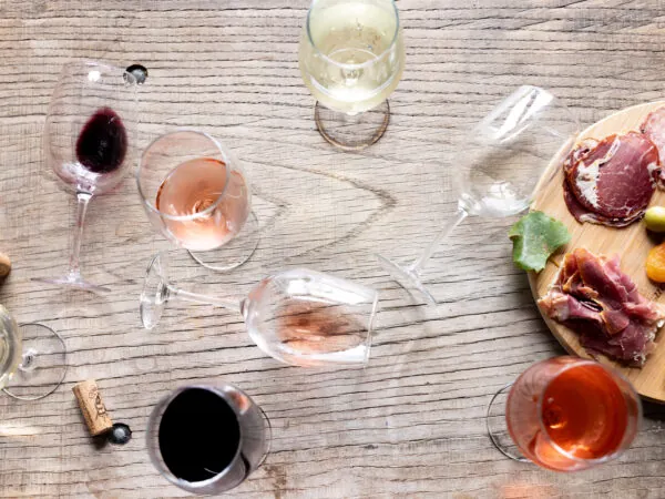 An overhead shot of a wooden table with several glasses of red, white, and rosé wine arranged around a wine carafe.