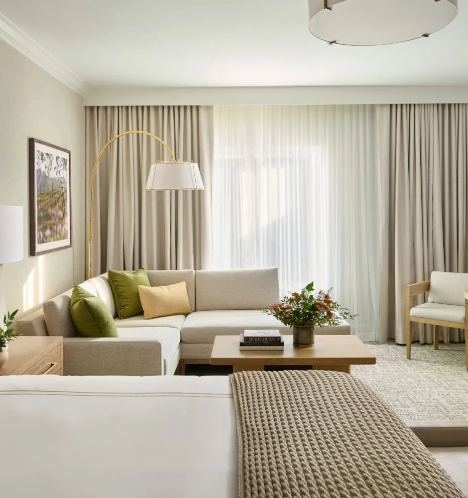 Spacious hotel suite with bed, sofa, and natural light
