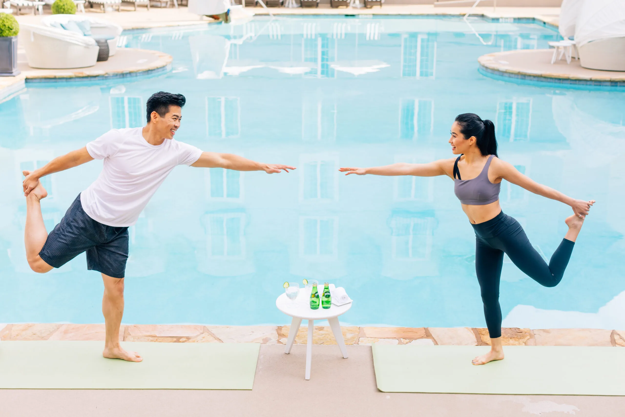 Man and woman doing yoga poses by pool