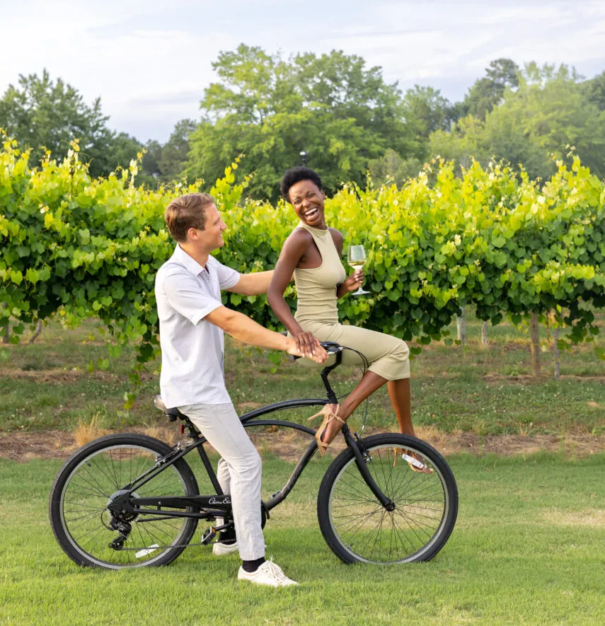 A happy couple on a bike in a vineyard. The woman is sitting on the handlebars, laughing.