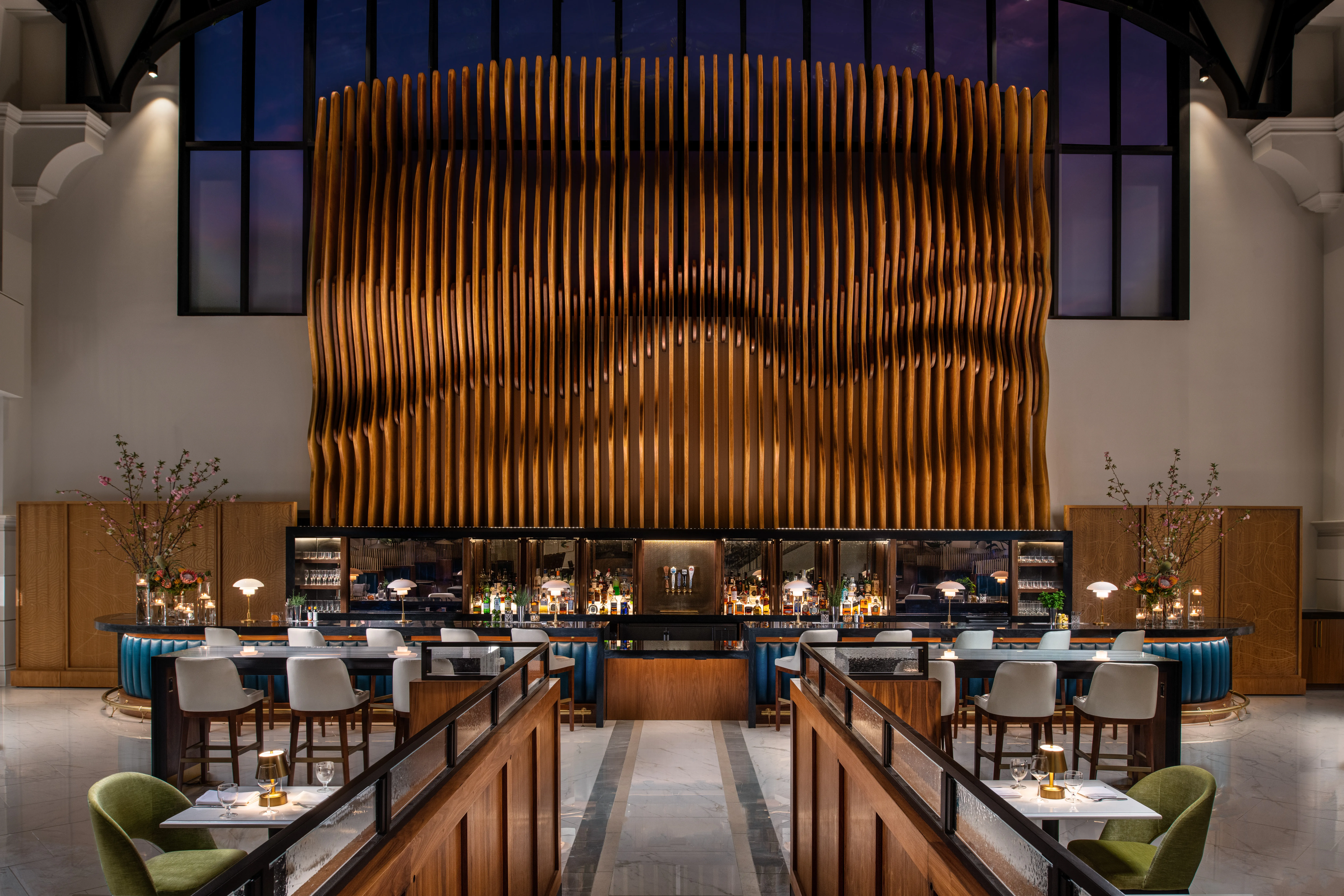 A long, modern dining hall with rows of tables and chairs facing a large, textured wooden wall.