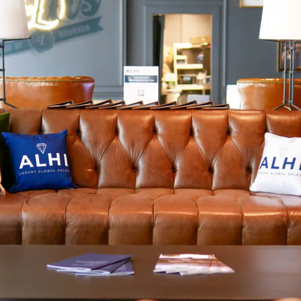 A brown leather couch with a blue pillow that says "ALHI," next to a small table with bottles and a box.