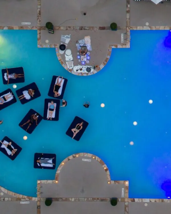 An aerial view of a swimming pool with bright blue lights and people on inflatable rafts.