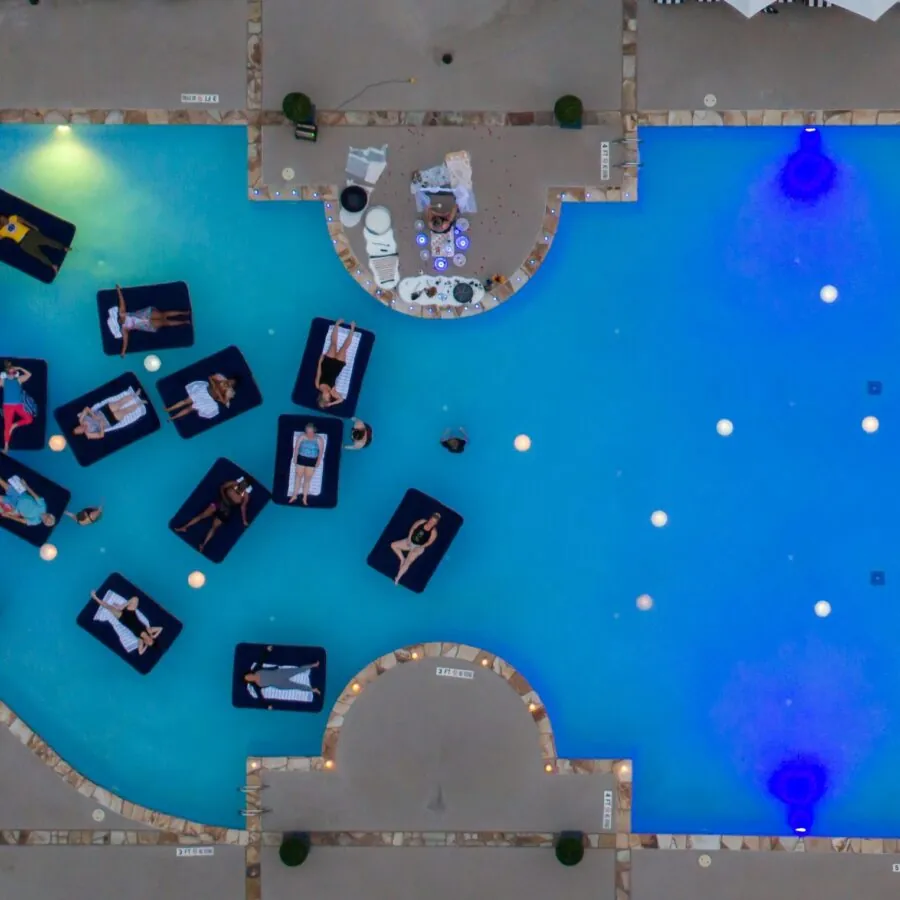 An aerial view of a swimming pool with bright blue lights and people on inflatable rafts.