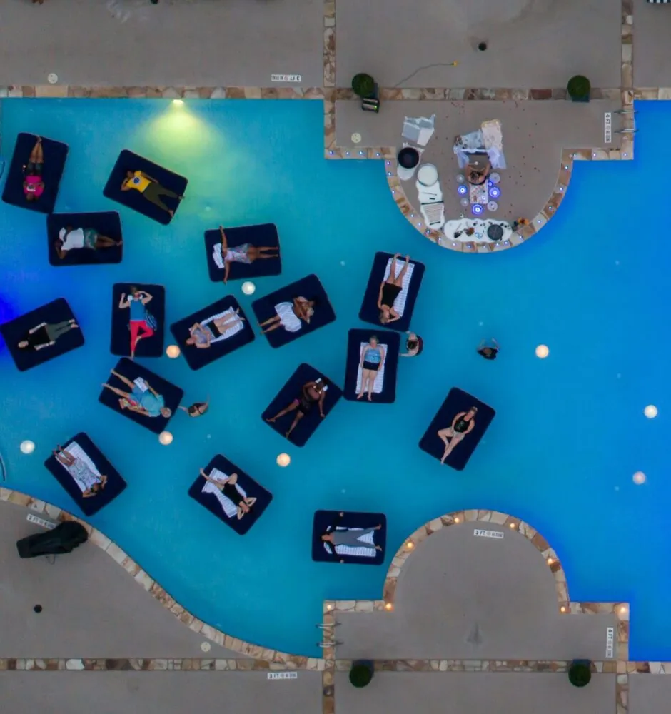 An aerial view of a swimming pool with bright blue lights and people on inflatable rafts.