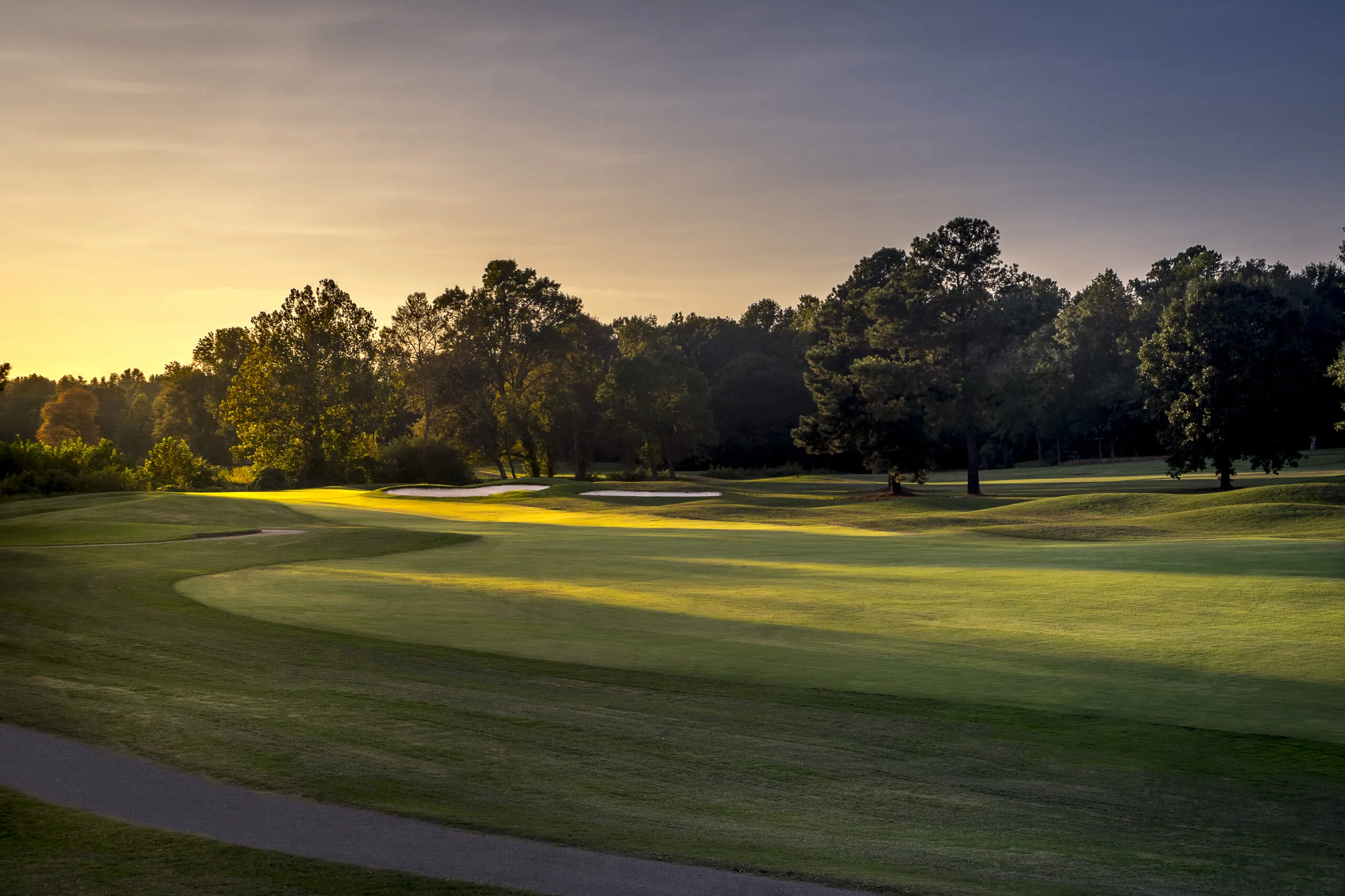 A golf course with green grass and trees in the warm light of a sunset.