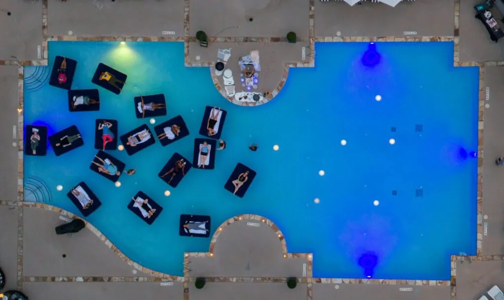 An aerial view of a swimming pool with multiple inflatable lounge floats shaped like cars.